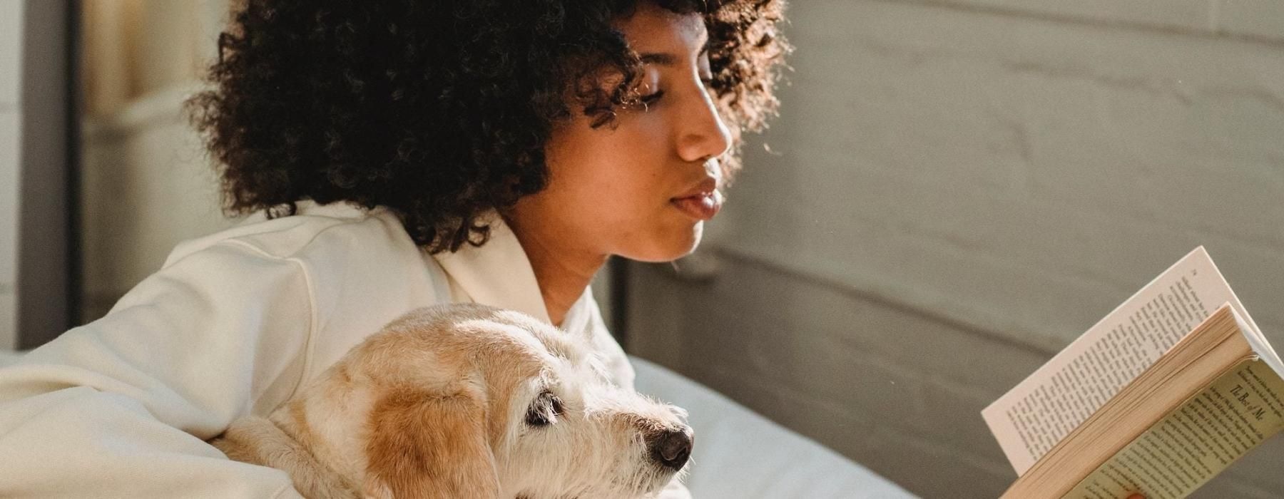 a person reading a book while laying next to a dog